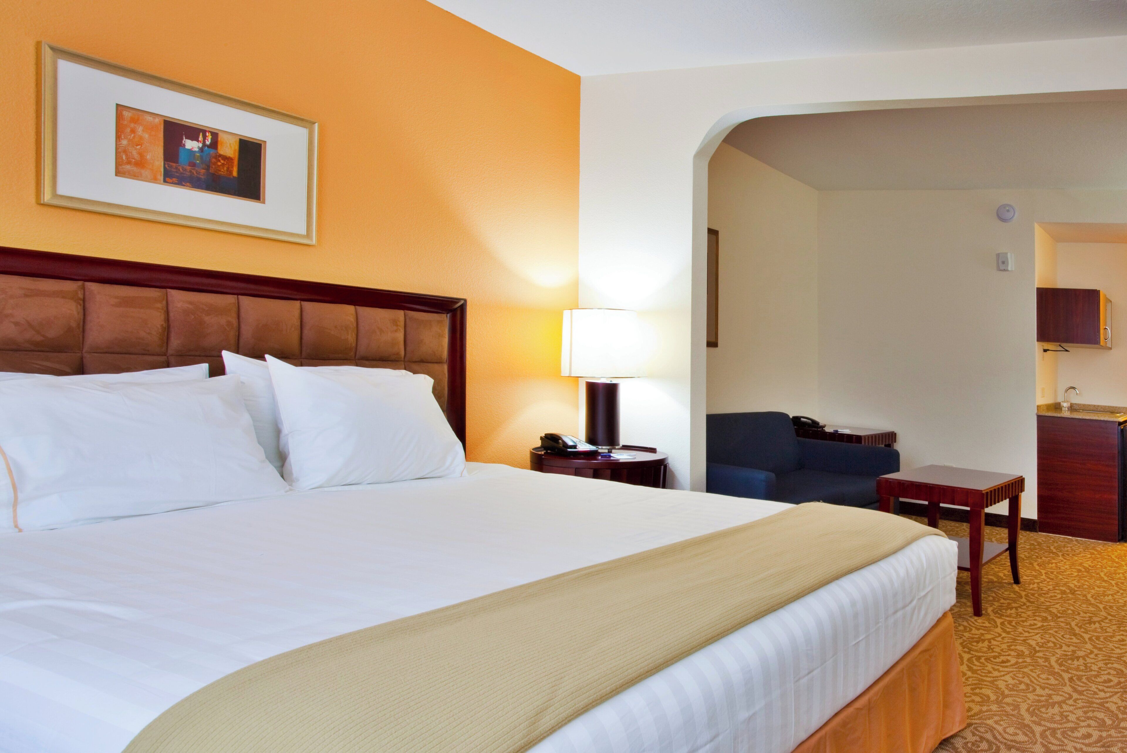 Een hotelkamer met een groot bed, een bedlampje, een bureau met telefoon en een stoel.
