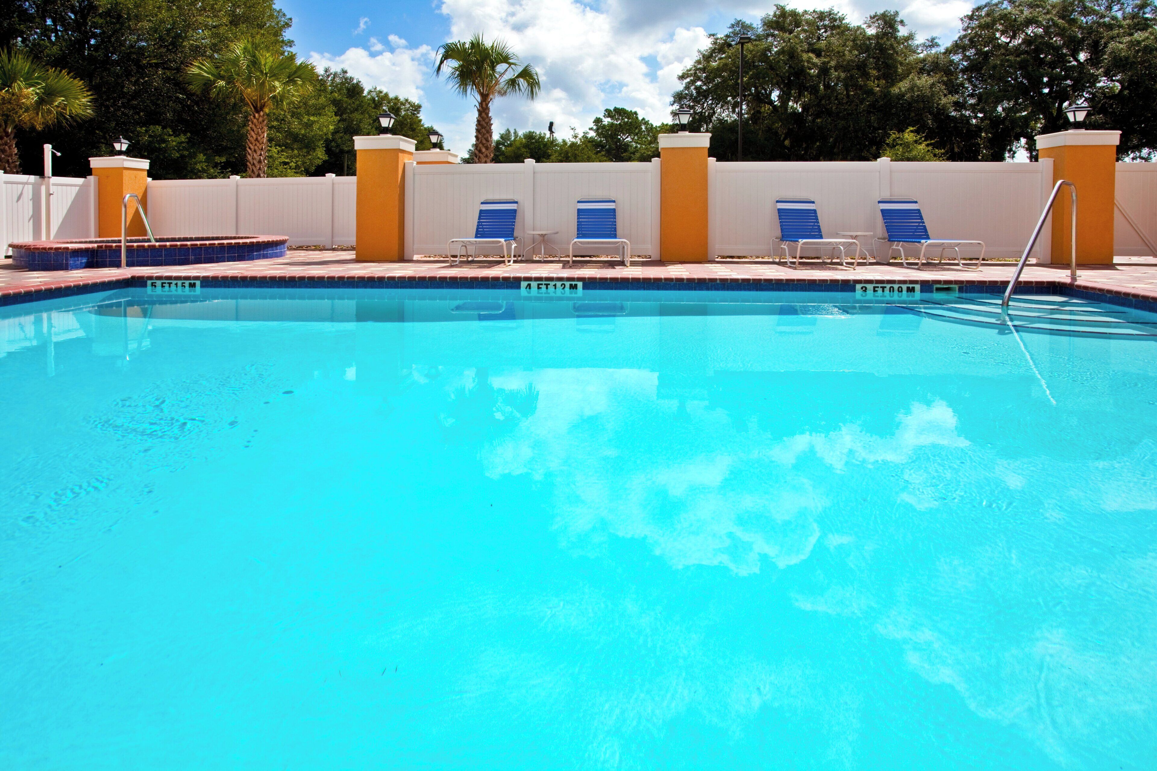 A clear swimming pool with blue water, surrounded by a white fence and palm trees.