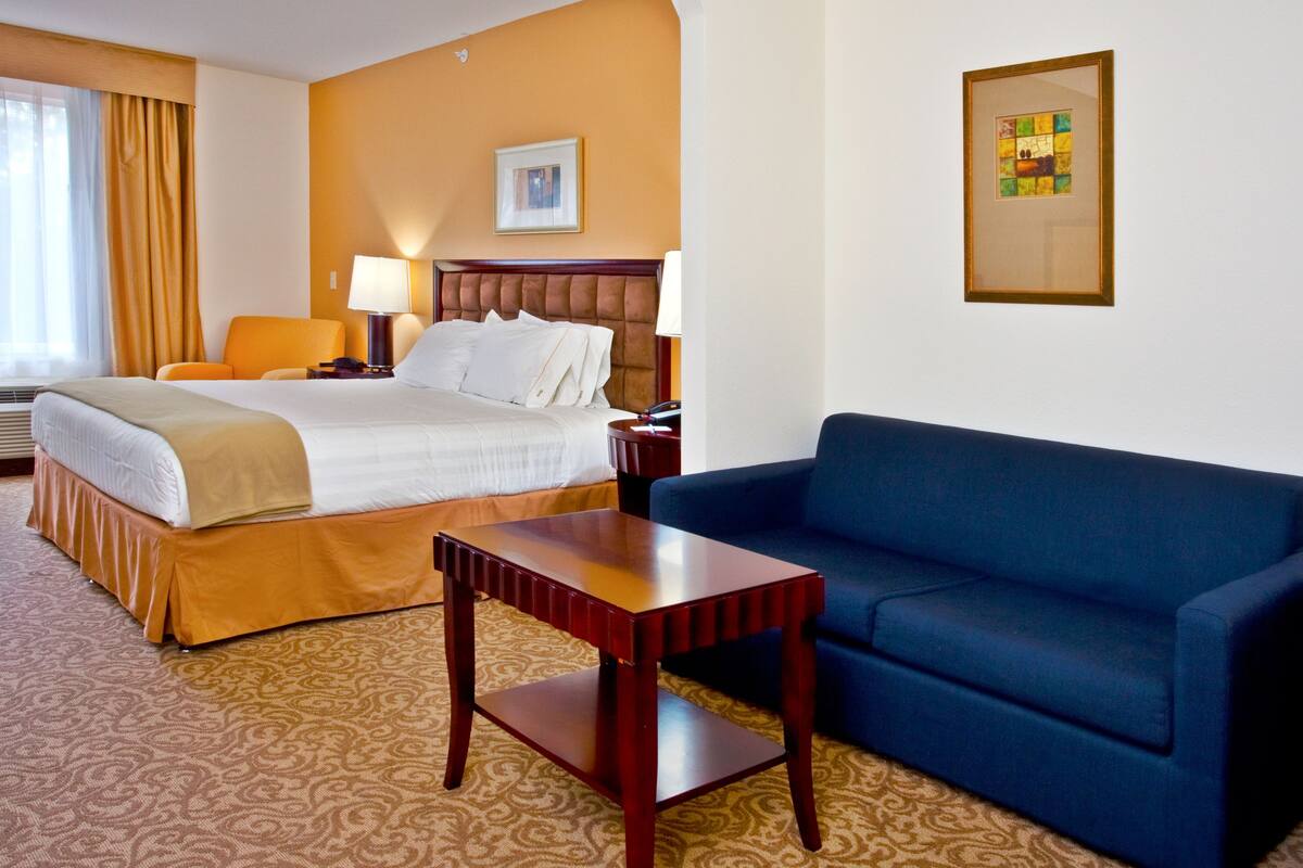 A hotel room with a bed, a blue sofa, a wooden table, and a patterned carpet.