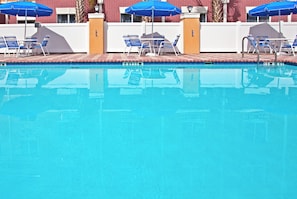 A swimming pool with blue chairs and umbrellas, surrounded by a white fence and a red brick building. - Holiday Inn Express Hotel & Suites Brooksville by IHG (Brooksville)