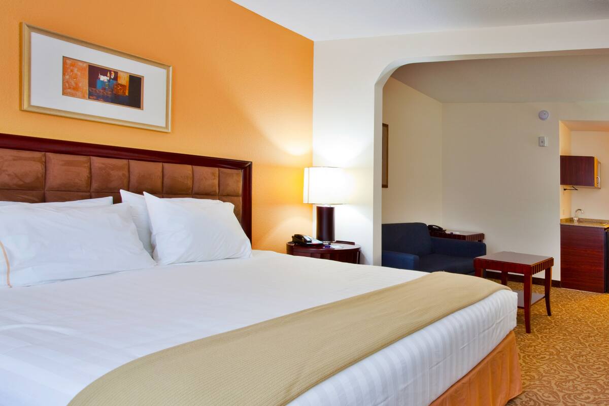 A hotel room with a large bed, a desk, a chair, and a small kitchenette.