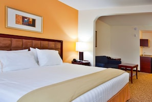 A hotel room with a large bed, a desk, a chair, and a small kitchenette.