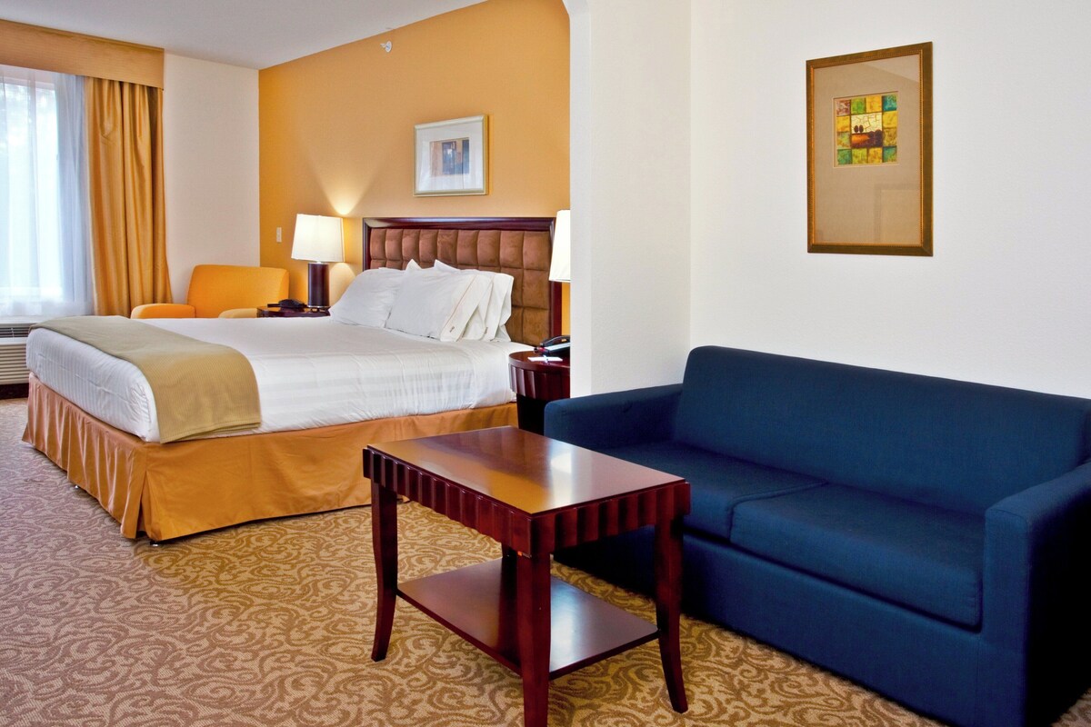 A hotel room with a bed, bedside tables, a desk, a sofa, and a framed picture on the wall.