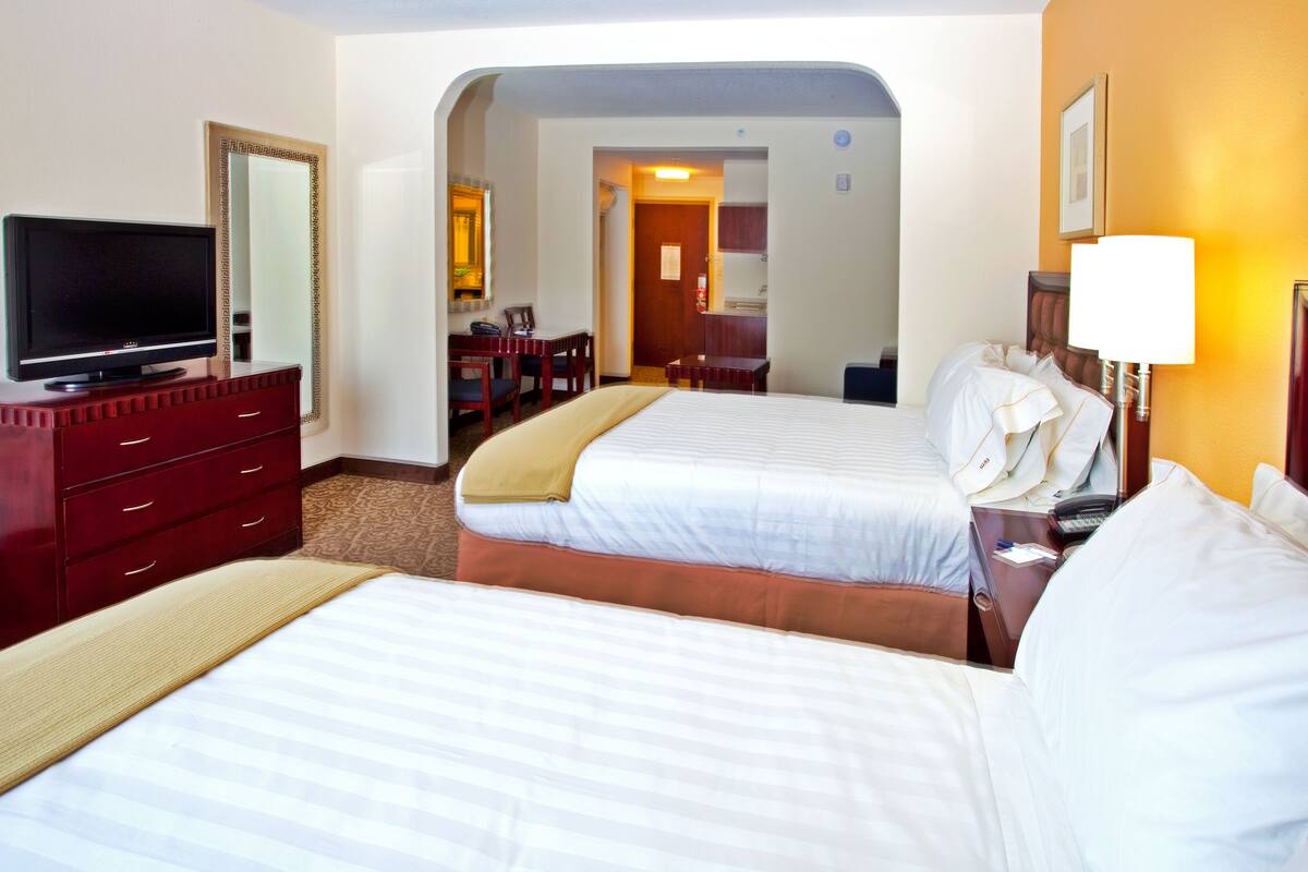 A hotel room with two beds, a TV, a desk, and a bathroom visible through an archway.