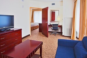 A hotel room with a television, a desk, a chair, a sofa, and a bed.