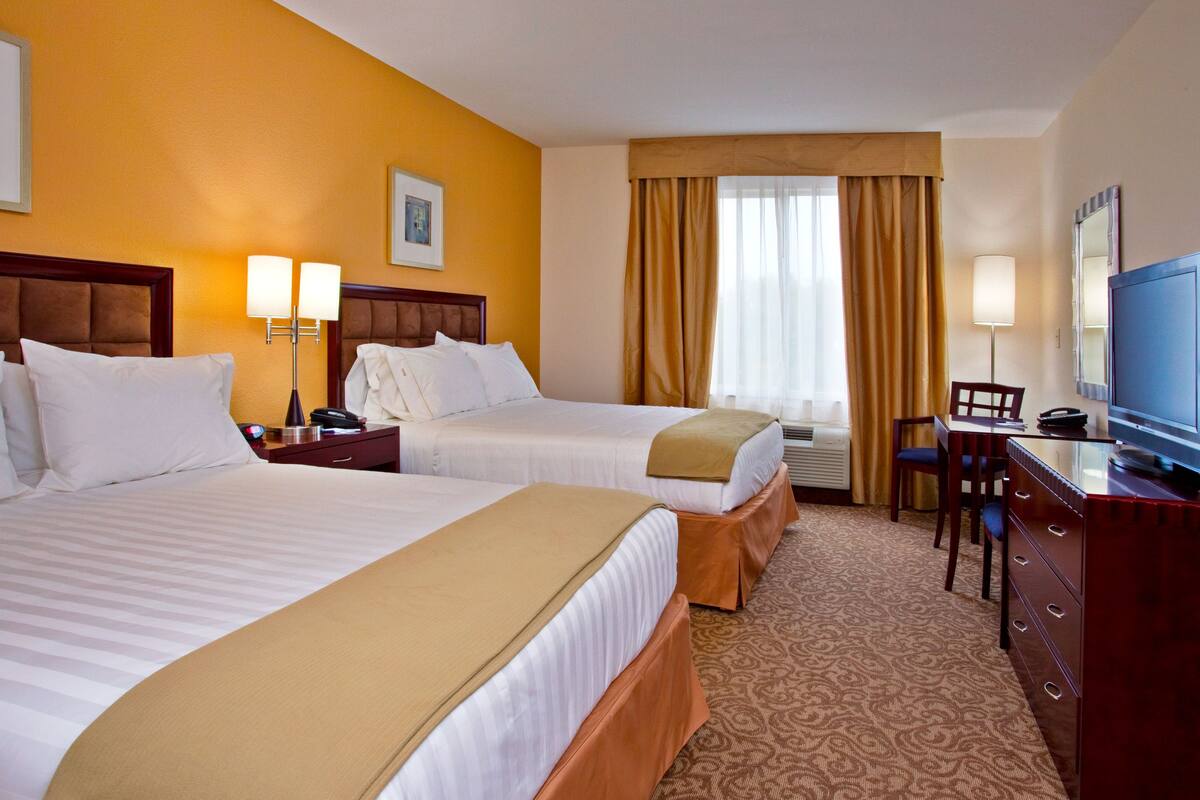 A hotel room with two beds, a desk, a chair, a television, and a window with curtains.