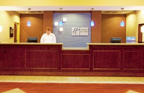 A hotel reception desk with a receptionist, a Holiday Inn Express sign, and a Priority Club sign. - Holiday Inn Express Hotel & Suites Brooksville by IHG (Brooksville)