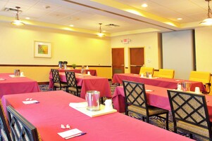 Un salón de conferencias con mesas dispuestas para reuniones, equipado con tarjetas de identificación, bolígrafos y jarras de agua.