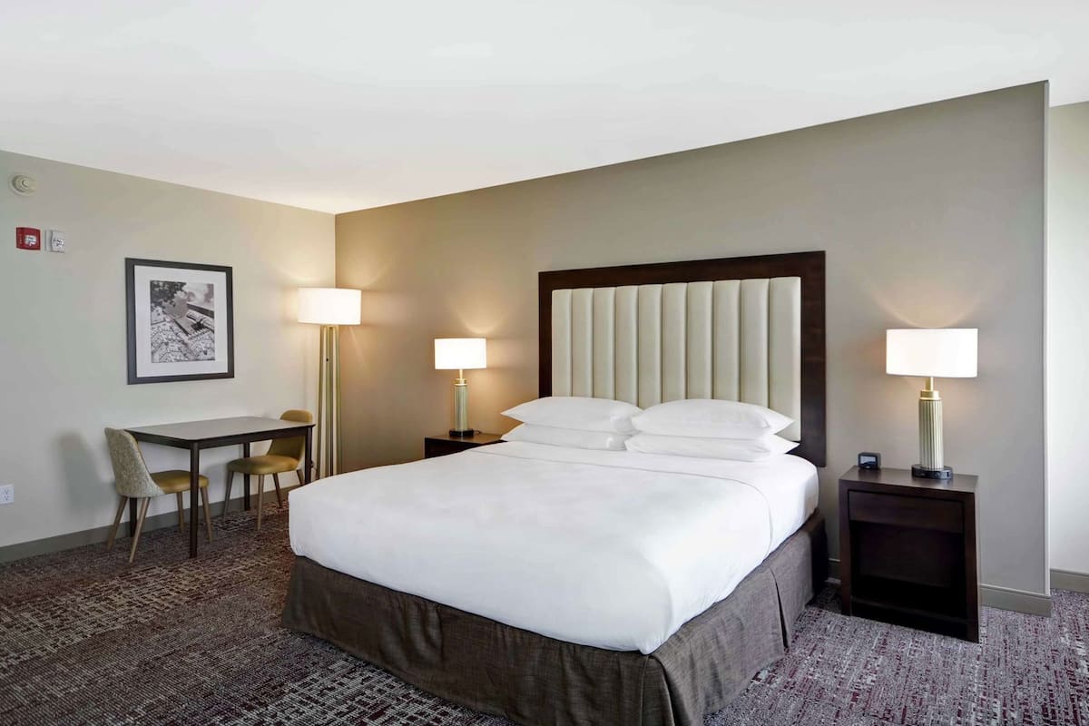 A hotel room with a bed, bedside tables, a desk, and chairs.