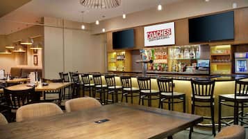 Een restaurant met een bar, houten tafels en stoelen, en een bordje met de tekst 'COACHES SPORTS BAR & GRILL'.