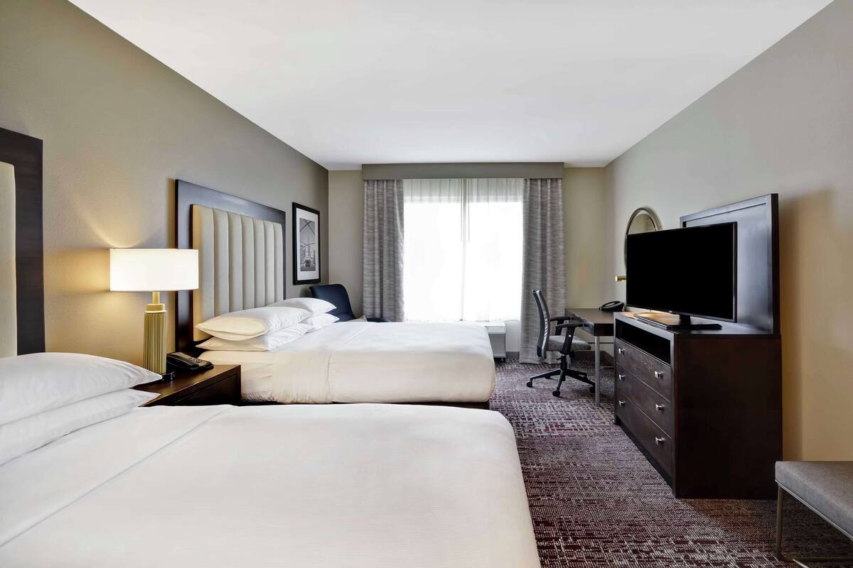 A hotel room with two beds, a desk, a television, and a dresser.