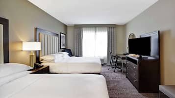 A hotel room with two beds, a desk, a television, and a dresser.