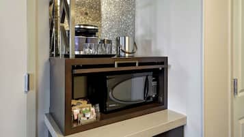 Una kitchenette compacta con microondas integrado, cafetera y refrigerador pequeño.