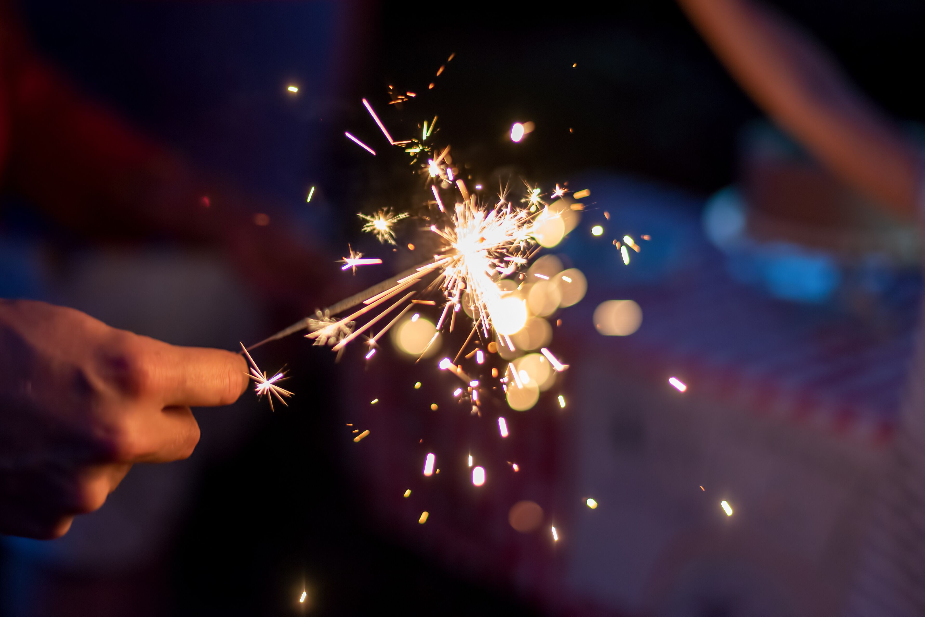 A hand holding a sparkler with visible sparks and light effects.