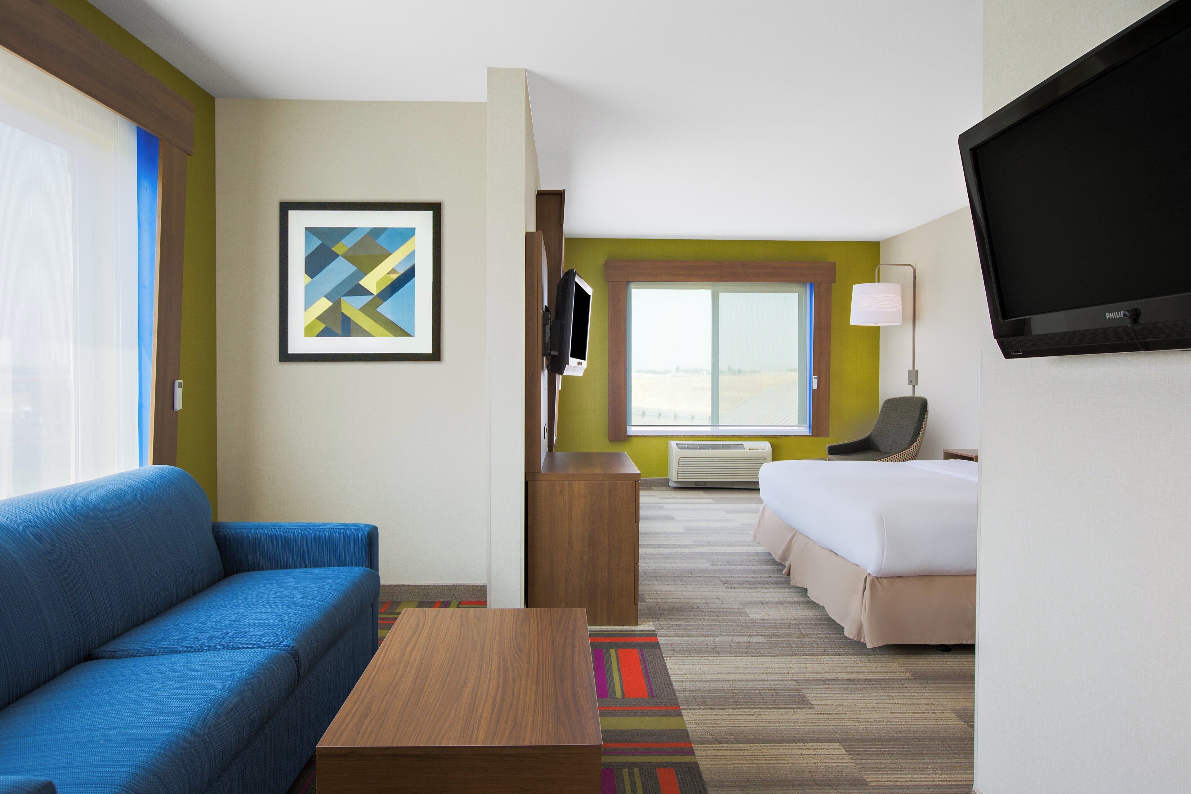 A hotel room with a blue sofa, a bed, a television, and a window with a view.