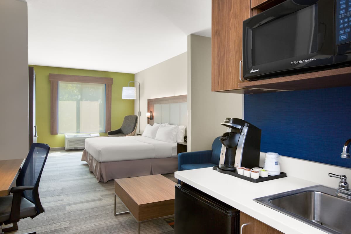 Habitación de hotel con cama, escritorio, silla, microondas, cafetera y lavabo.