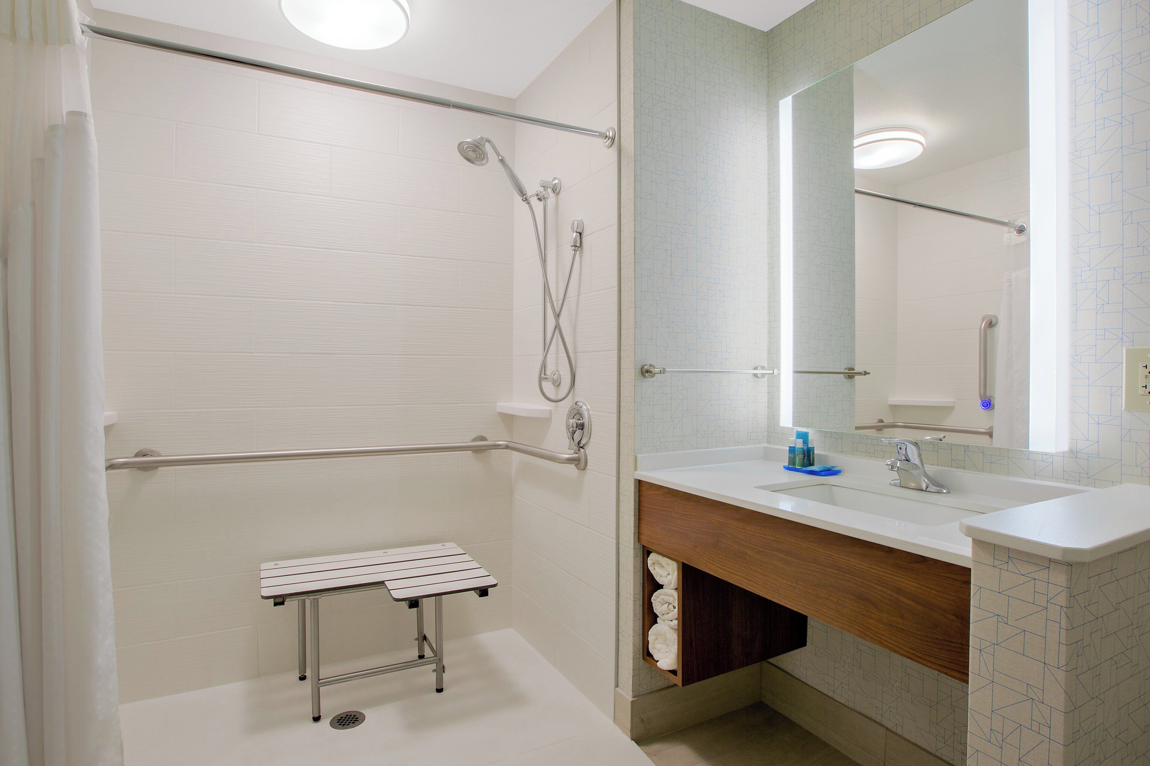 A bathroom with a shower, a sink, a mirror, and a towel rack.