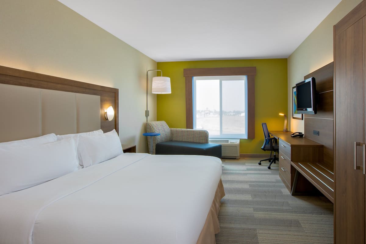Habitación de hotel con una cama grande, un escritorio con ordenador, televisión y ventana con vistas.