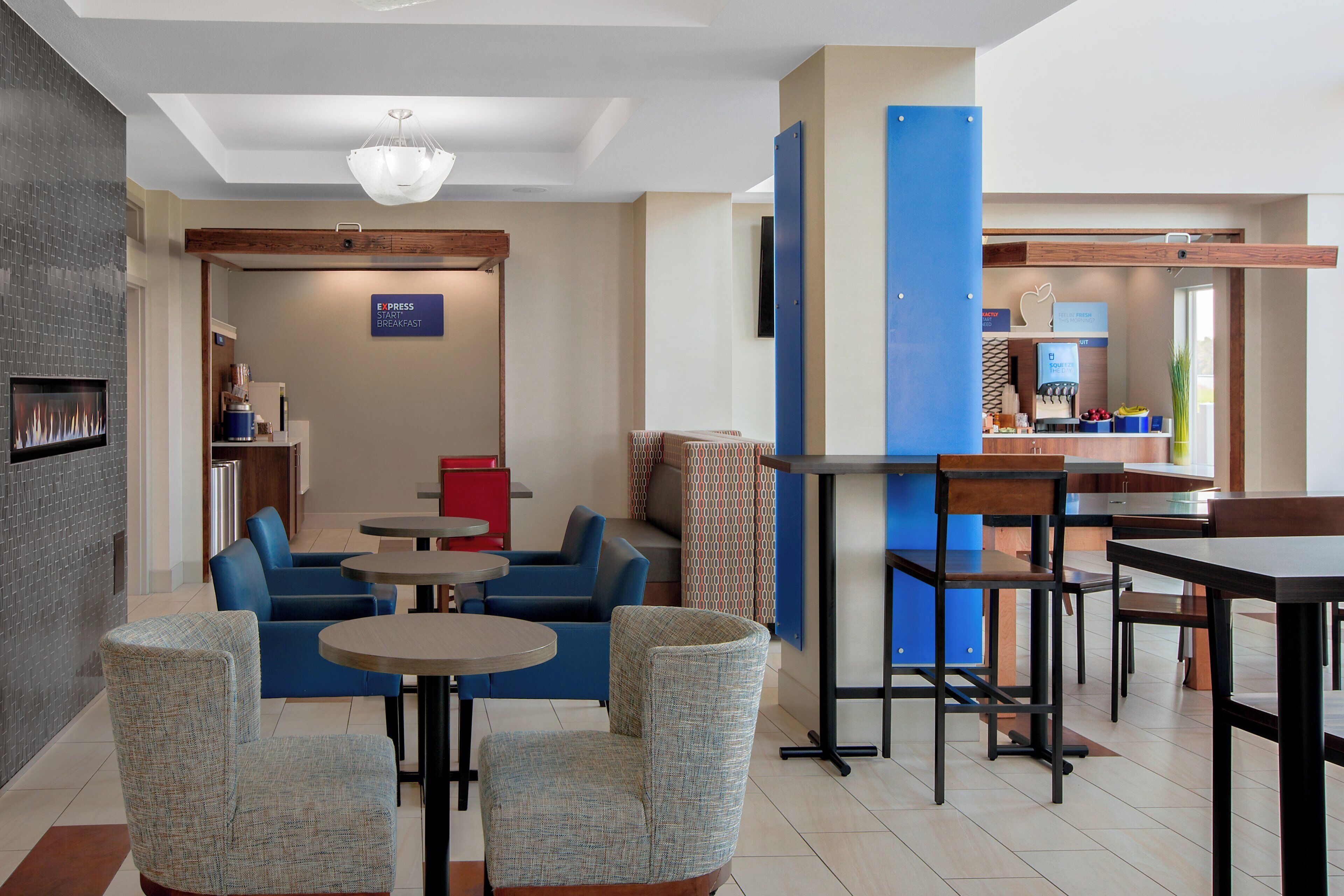 A hotel lobby with seating areas, a fireplace, and a breakfast sign.
