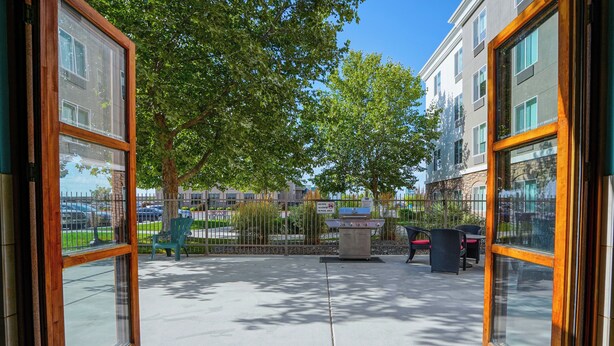 An outdoor patio area with a barbecue grill, seating, and a view of a residential building.