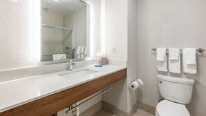 Une salle de bain avec un lavabo blanc, un meuble-lavabo en bois, un miroir, des toilettes et un porte-serviettes.