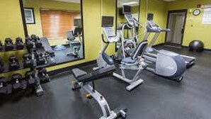 Une salle de sport équipée de matériel d’exercice, d’un miroir et d’une horloge fixée au mur.