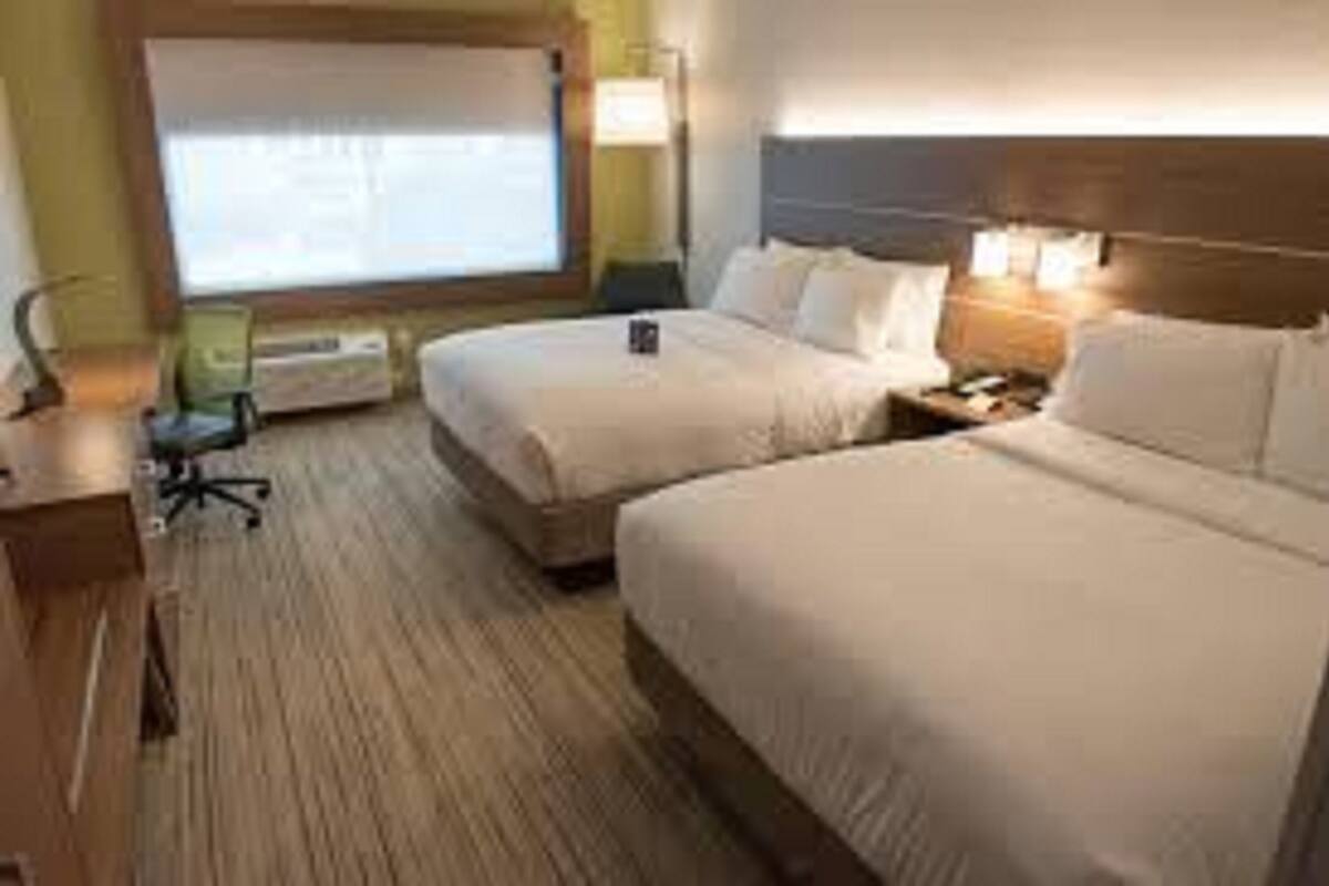 A hotel room with two beds, a desk, a chair, and a window with blinds.