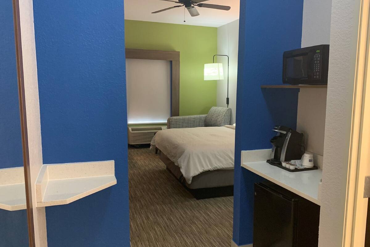 A hotel room with a bed, a desk with a coffee maker, a microwave, and a ceiling fan.