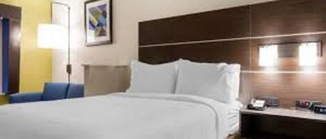 A hotel room with a large bed, a bedside table with a lamp, and a painting on the wall.