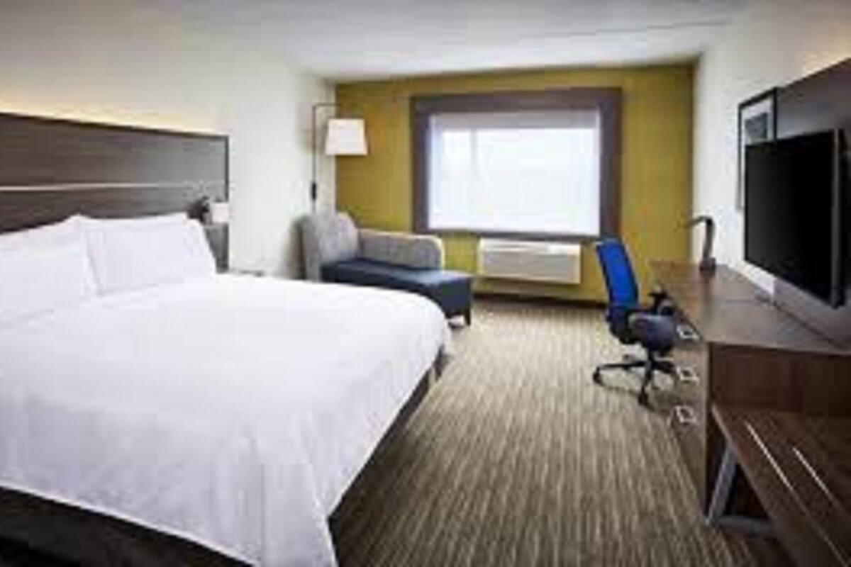 A hotel room with a large bed, a desk with a computer, a chair, and a window with blinds.