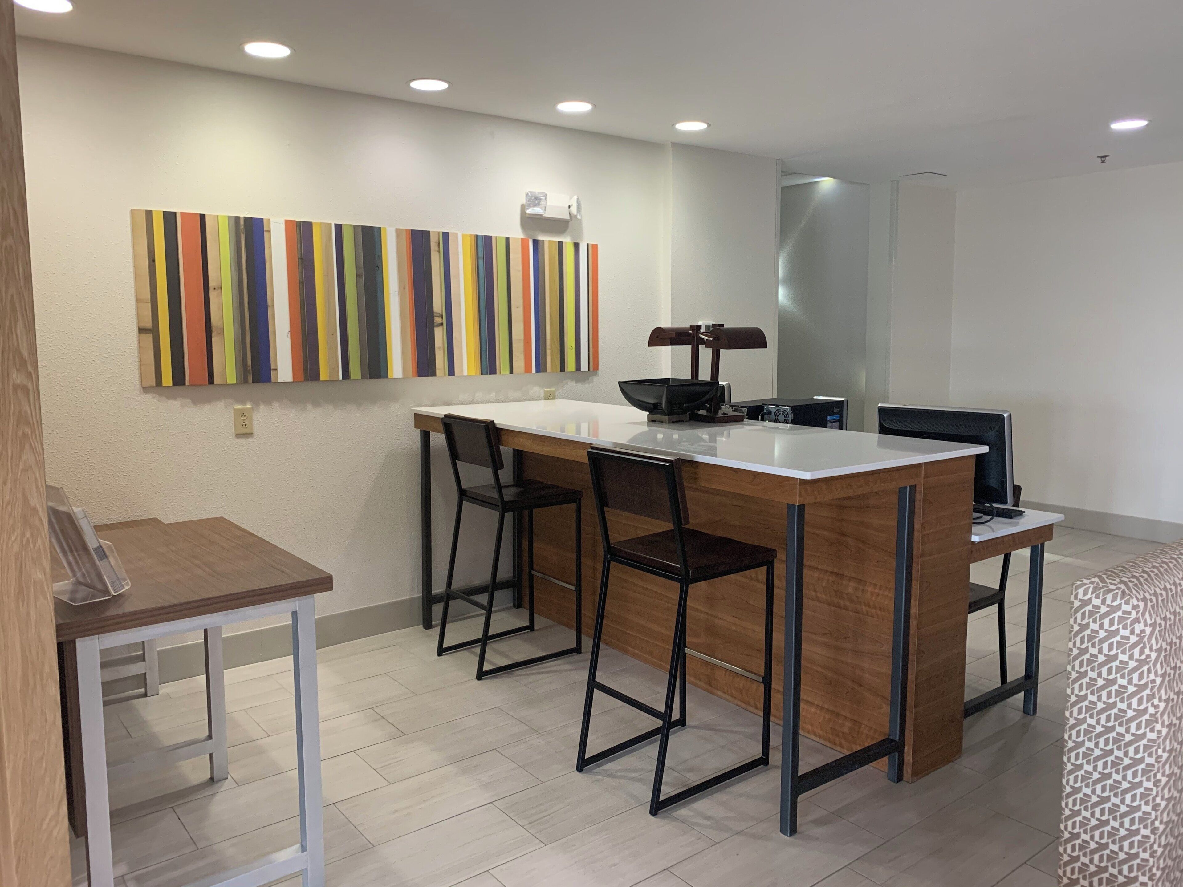 A modern kitchen with a central island, bar stools, and a colorful striped wall art piece.