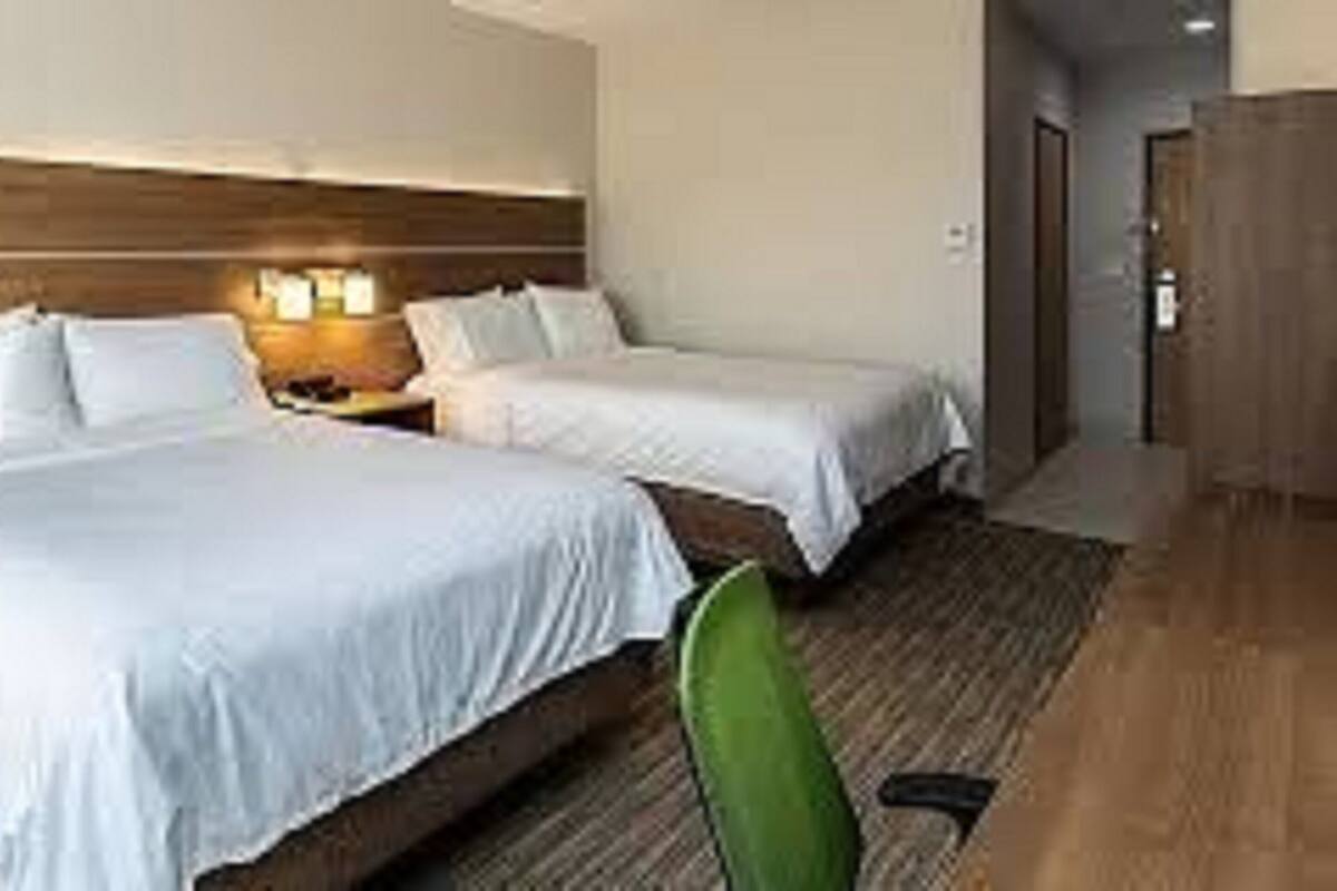 A hotel room with two beds, a wooden headboard, and a nightstand with lamps.