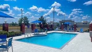 Une piscine entourée d’un mur de briques et d’une clôture, avec des chaises longues et des parasols.