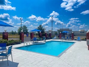 A swimming pool with lounge chairs and umbrellas, surrounded by a brick wall and a fence. - Holiday Inn Express McComb by IHG (McComb)