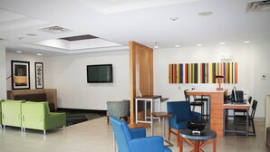 Un hall d’entrée moderne avec un canapé vert, des fauteuils bleus, une cloison en bois et un téléviseur fixé au mur.