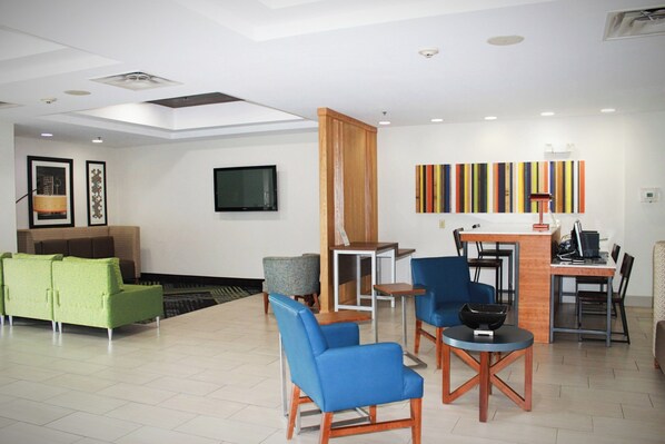 A modern lobby with a green sofa, blue chairs, a wooden partition, and a TV mounted on the wall. - Holiday Inn Express McComb by IHG (McComb)