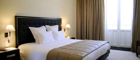 A neatly made bed with a black headboard, two bedside lamps, and a window with curtains.