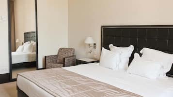 Habitación de hotel con una cama grande, una silla, una mesita de noche, una lámpara y un espejo.