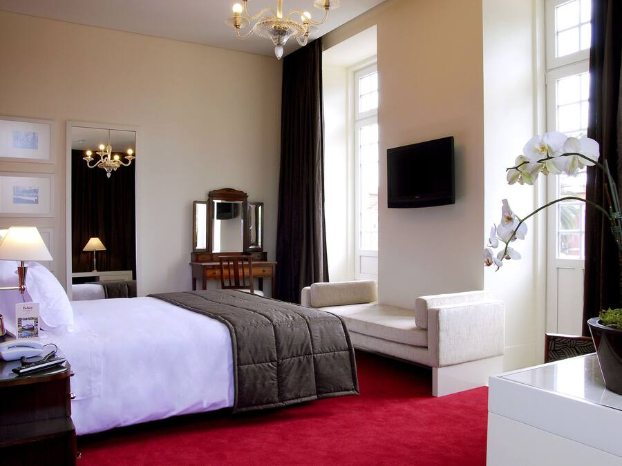 A hotel room with a large bed, a desk with a chair, a television, and a potted plant.