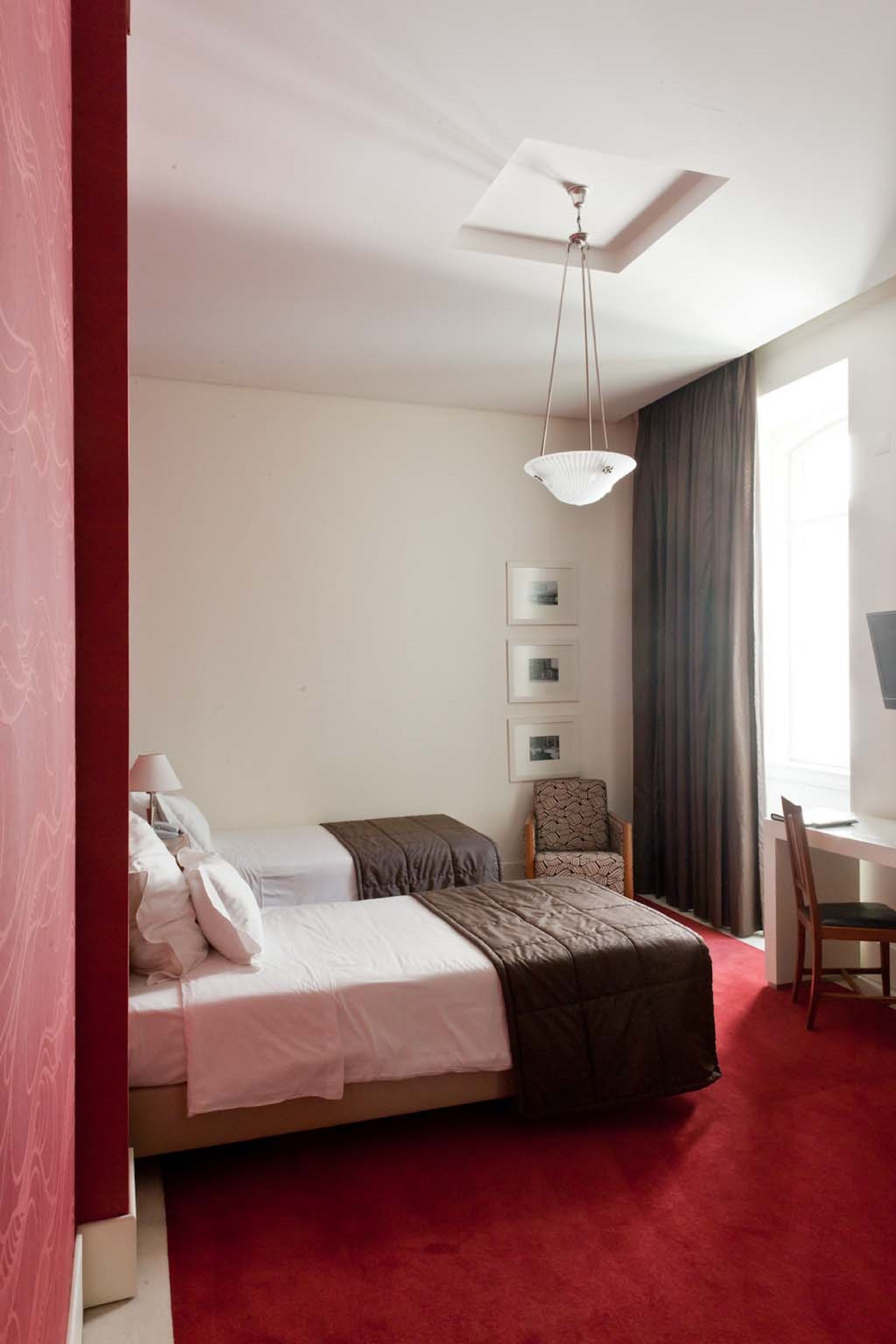 A hotel room with a bed, a desk, a chair, a ceiling fan, and a window with curtains.