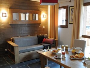 Una habitación acogedora con sofá, una mesa de comedor con provisiones para el desayuno y una ventana con cortinas.