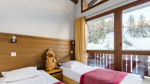 A hotel room with two beds, wooden headboards, a window with a view of a snowy landscape, and a teddy bear on one bed. - Résidence Lagrange Vacances Les Chalets Edelweiss (La Plagne-Tarentaise)