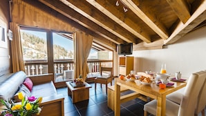 A cozy room with a wooden ceiling, a sofa, a dining table with breakfast items, and a TV on a stand. - Résidence Lagrange Vacances Les Chalets Edelweiss (La Plagne-Tarentaise)