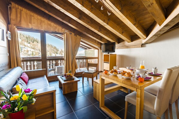 Una habitación acogedora con techo de madera, un sofá, una mesa de comedor con alimentos para el desayuno y un televisor sobre un mueble.