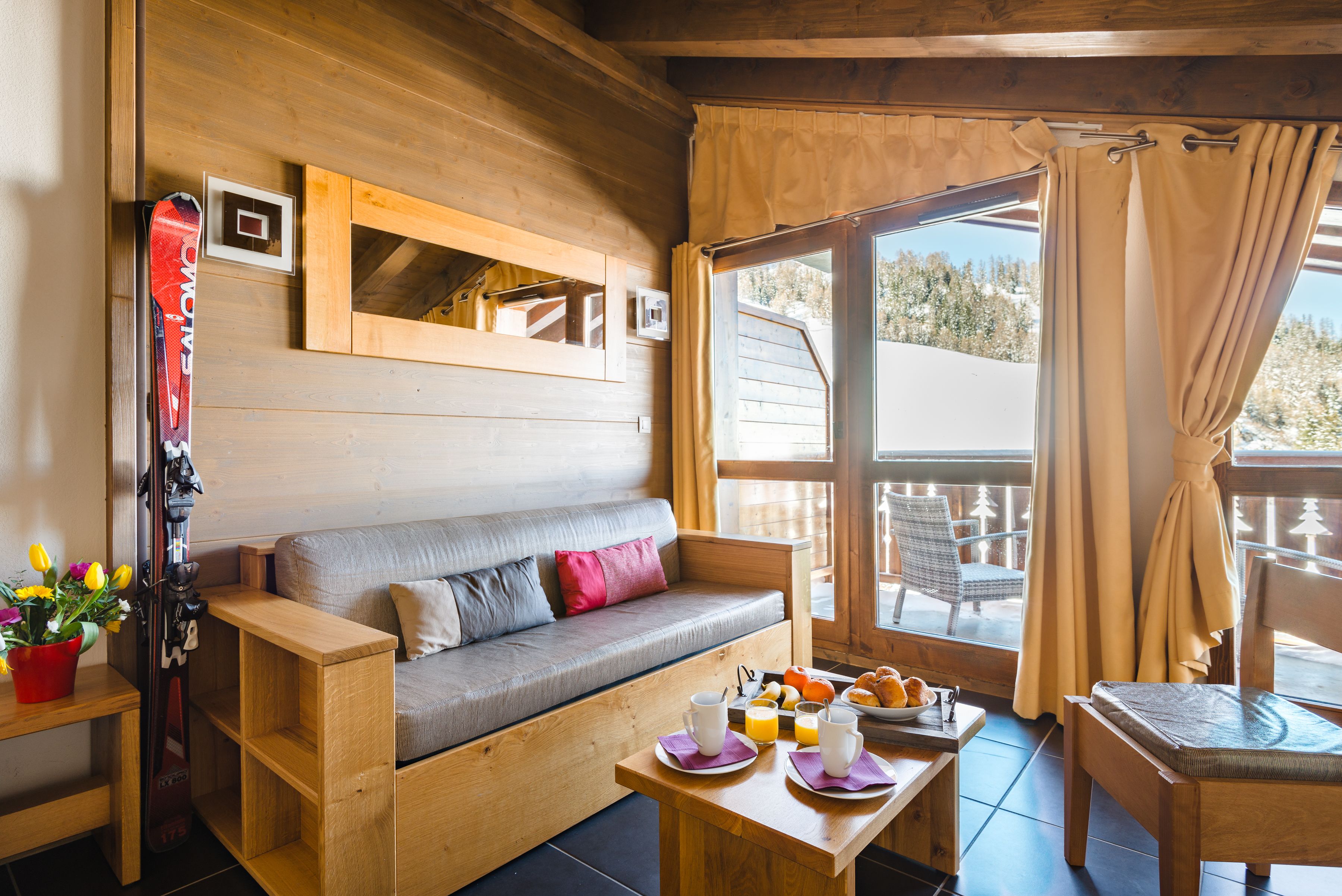 A wooden interior with a sofa, breakfast table, and ski equipment.