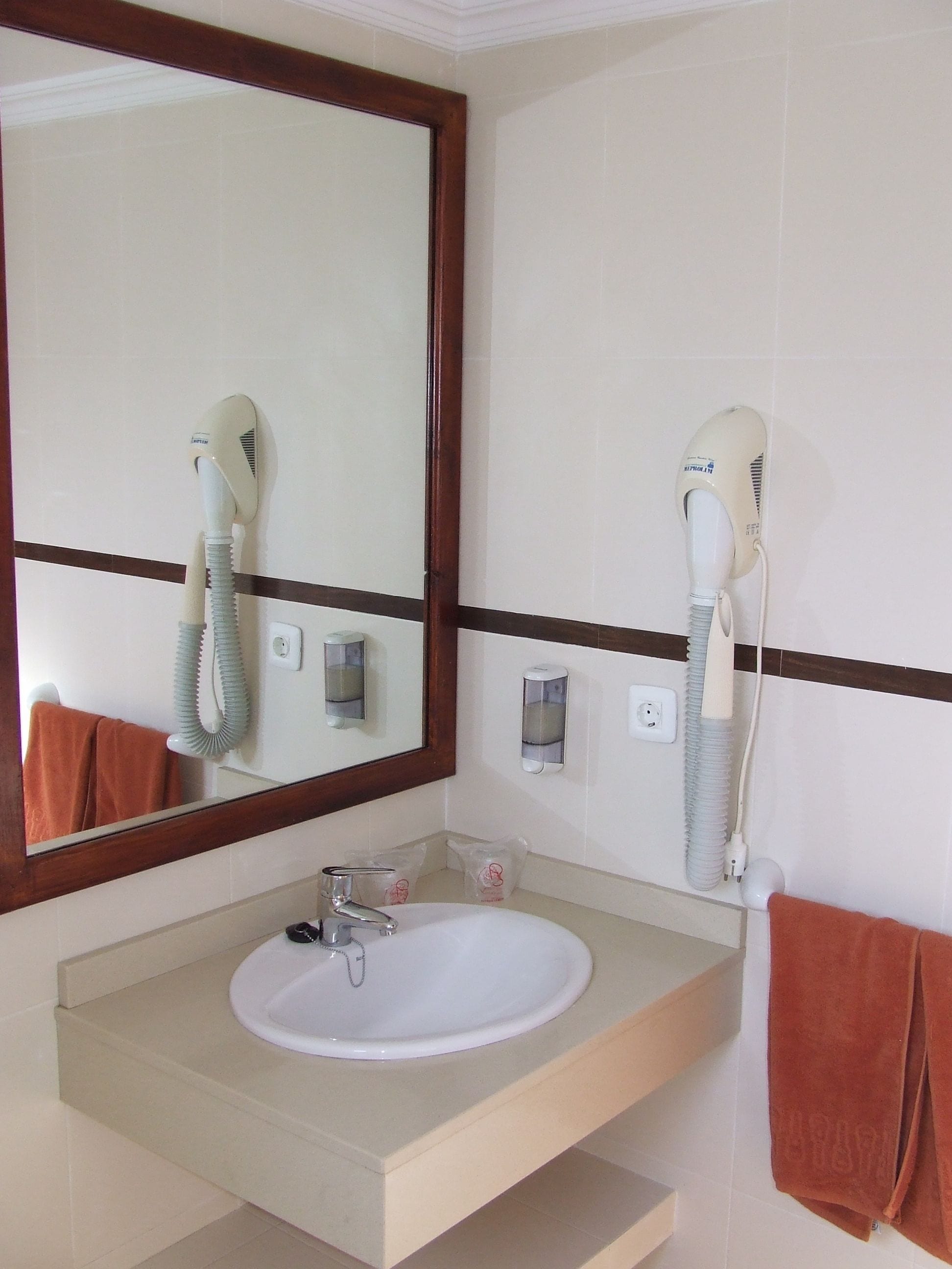 Une salle de bain équipée d’un lavabo, d’un miroir, d’un sèche-cheveux et d’un porte-serviettes.
