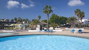A swimming pool with blue water, surrounded by lounge chairs and palm trees.