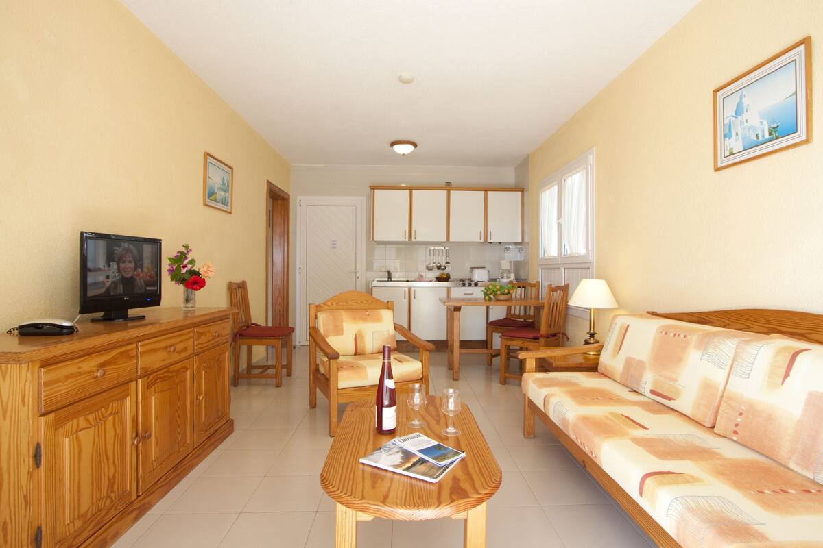 A living room with a wooden coffee table, a sofa, a TV, and a dining area with chairs and a table.