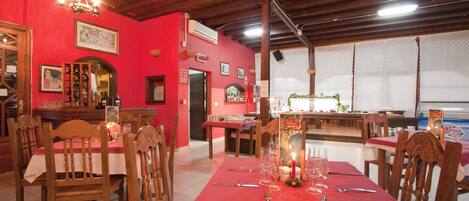 A dining area with wooden chairs and tables, red walls, and a chandelier.