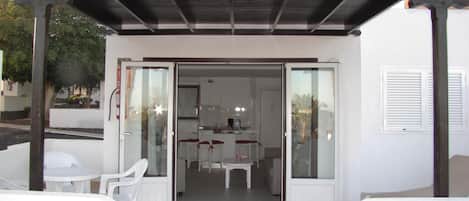 An open-plan living area with a kitchen, white furniture, and a glass door leading to the kitchen.
